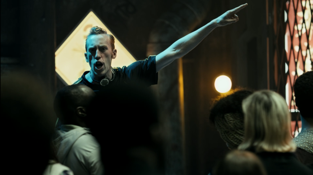 Still from the first episode of The  Expanse. A pale, skinny Belter speaking to a crowd and pointing for emphasis.